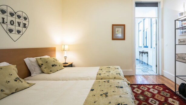 Une chambre d ’hôtel avec deux lits, une table de chevet avec une lampe, une décoration en forme de cœur sur laquelle est inscrit le mot « AMOUR », un tableau encadré accroché au mur et une vue sur l’extérieur par une porte ouverte.