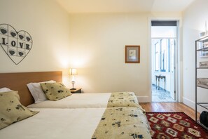 A hotel room with two beds, a nightstand with a lamp, a heart-shaped decoration with the word "LOVE", a framed picture on the wall, and a view of the outside through an open door.
