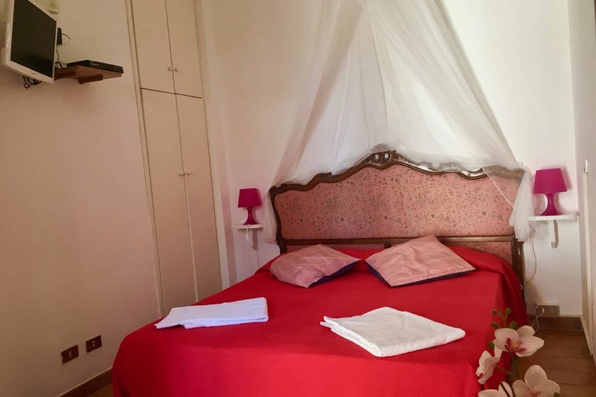Een keurig opgemaakt bed met een rode sprei, witte kussens, een houten hoofdbord en een witte hemel.