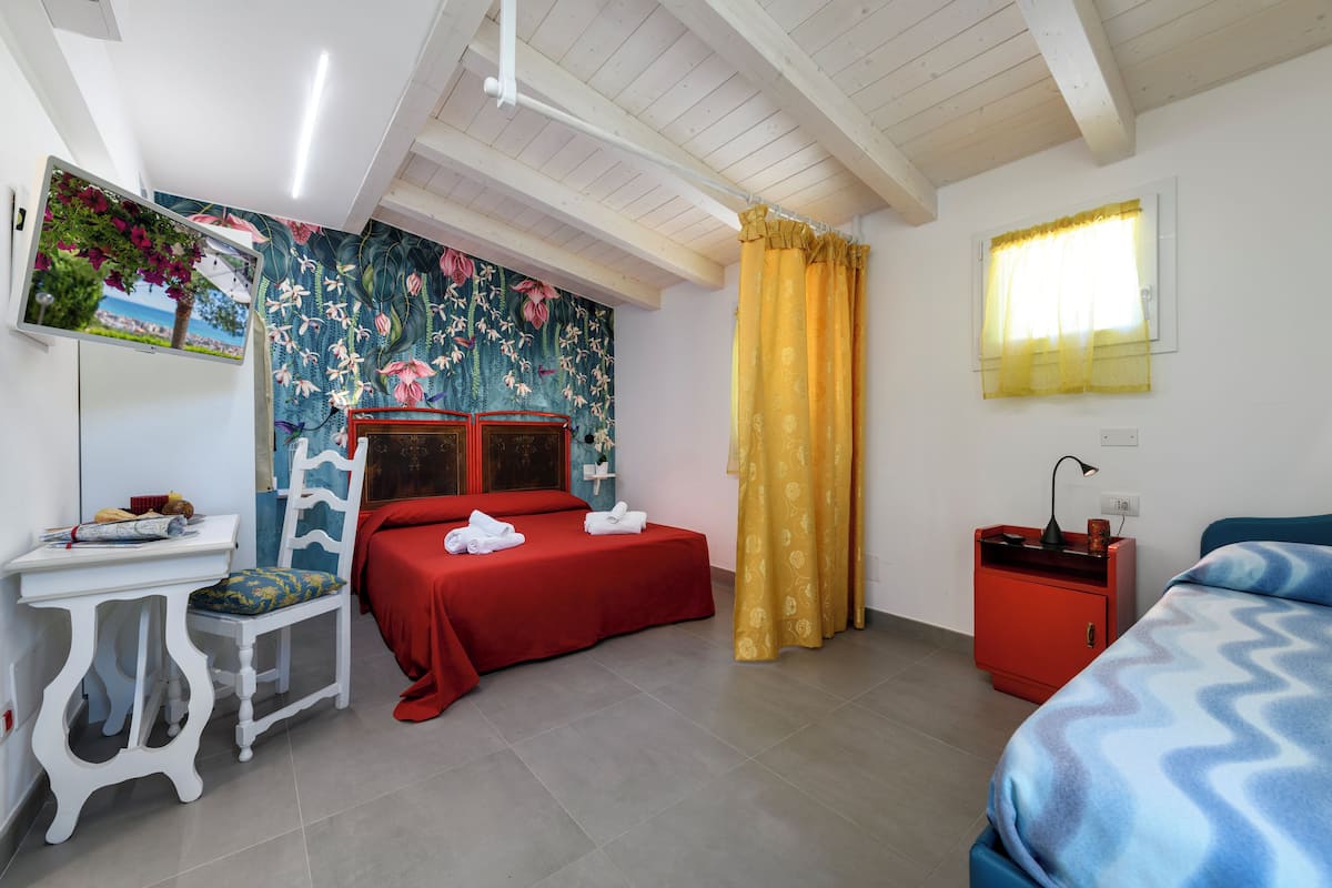 Een slaapkamer met een bed, bureau, stoel, nachtkastje en een raam met gordijnen.