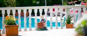 Een zwembadterras met een witte balustrade, plantenpotten en een klein beeldje.