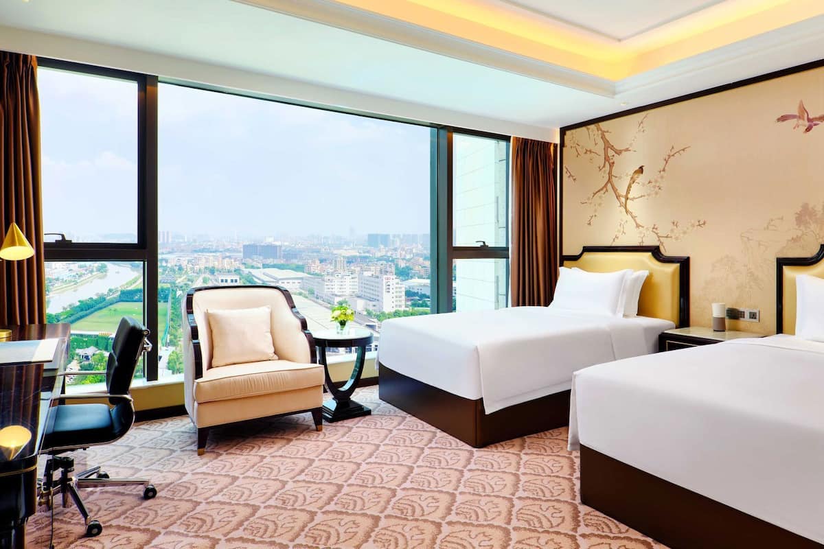 Une chambre d’hôtel avec deux lits, un bureau, une chaise et une grande fenêtre donnant sur la ville.