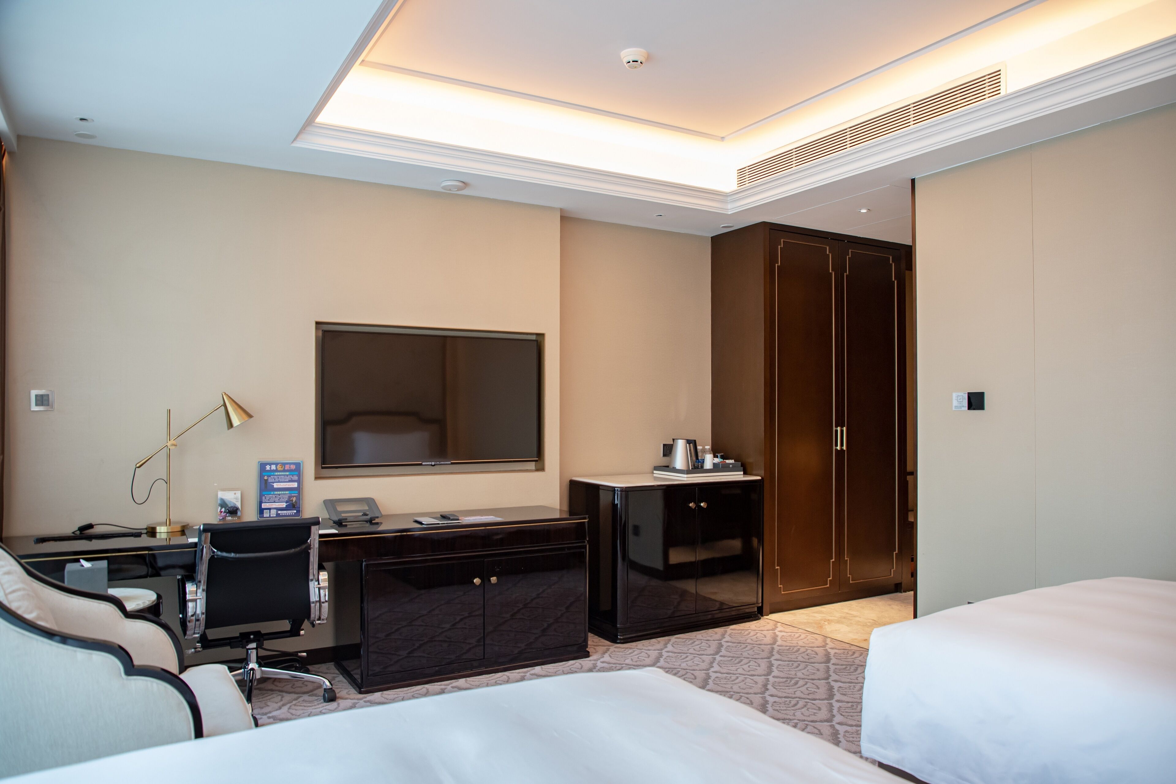 A hotel room with a desk, two beds, a wardrobe, and a large mirror.