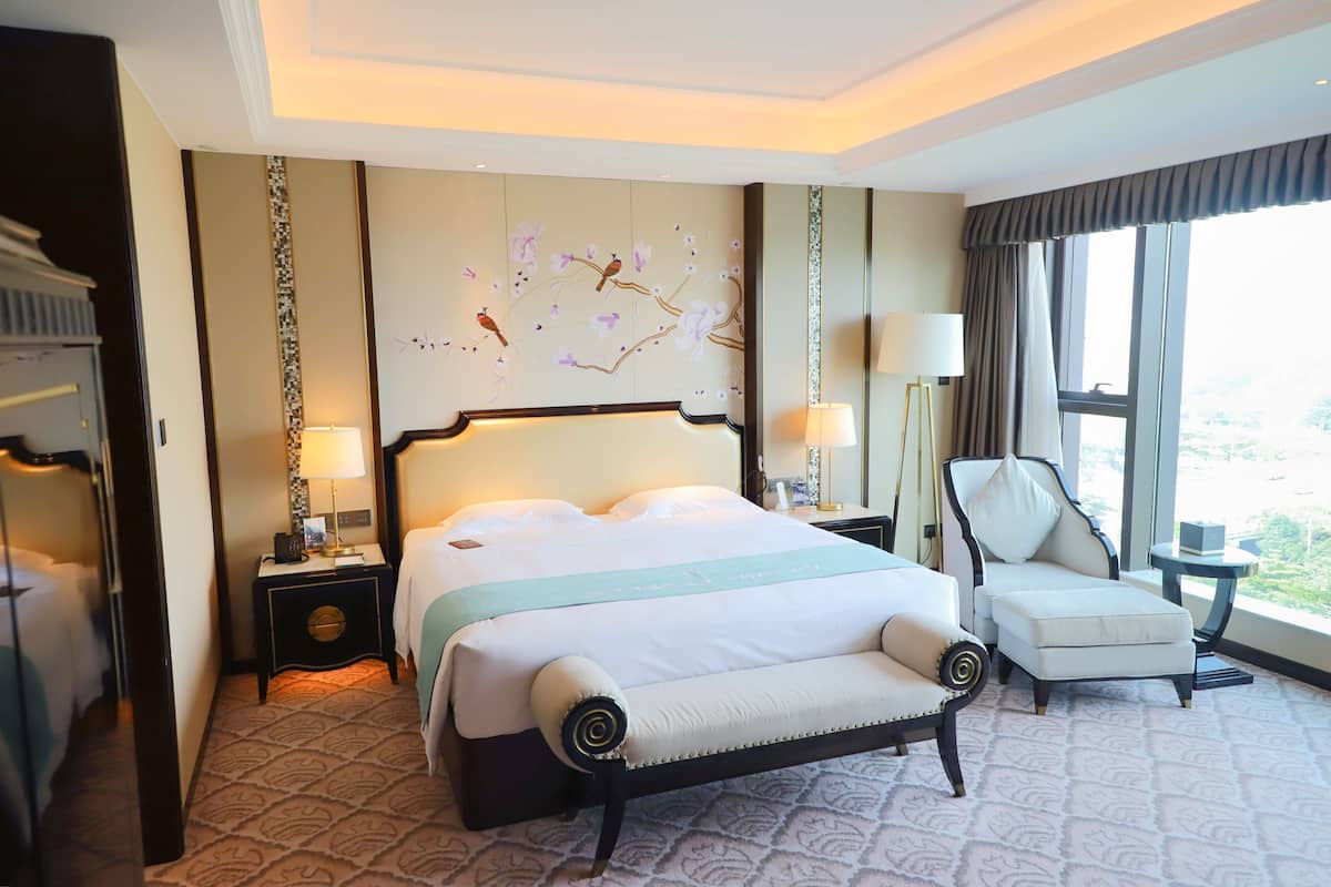 Une chambre d’hôtel dotée d’un grand lit, d’un coin salon, d’une table de chevet avec une lampe et offrant une vue sur l’extérieur.