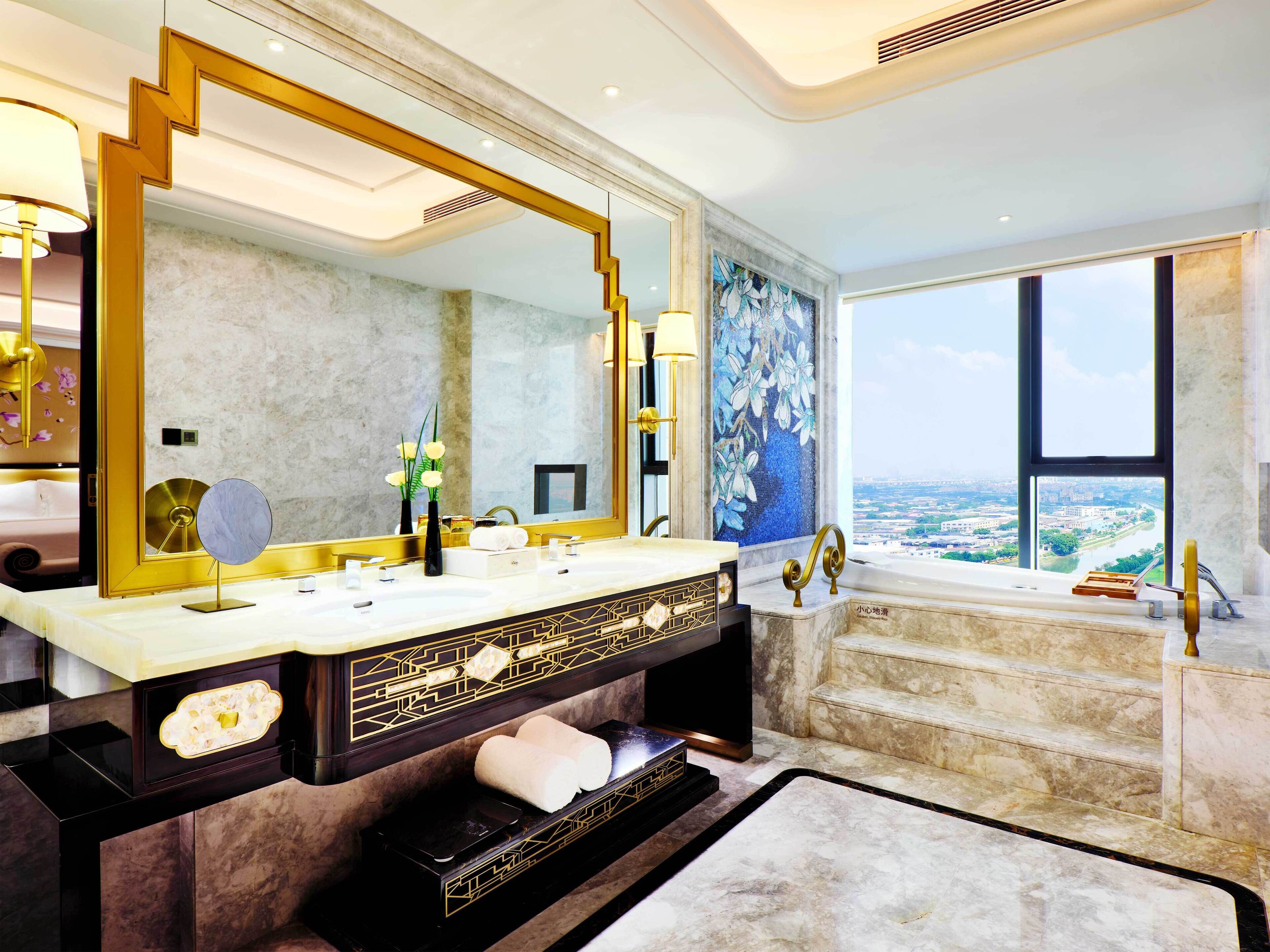 Ein luxuriöses Badezimmer mit großem Spiegel, zwei Waschbecken, einer Badewanne und Blick auf die Stadt.