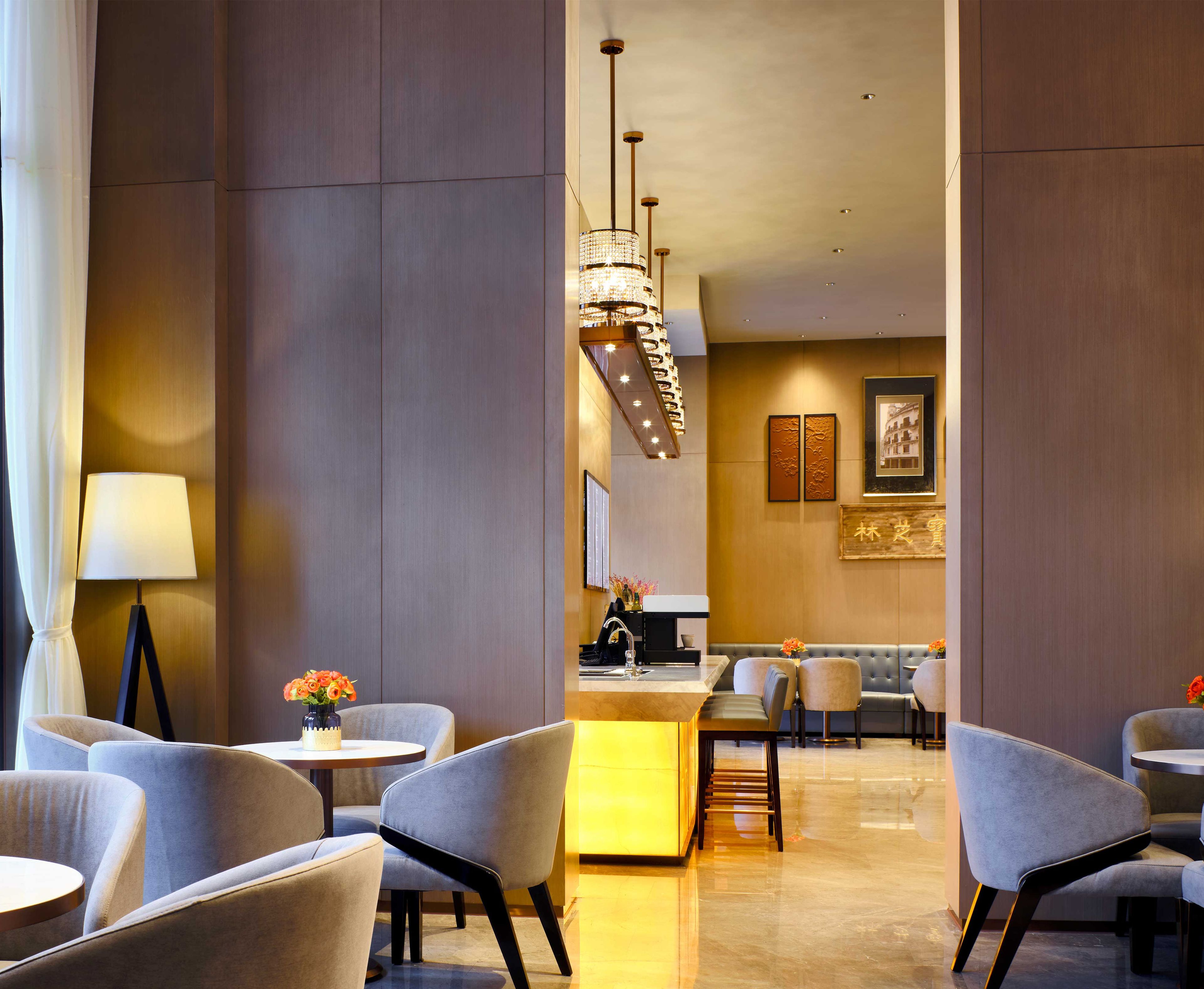A modern hotel lobby with a central bar, seating area, and decorative elements like a chandelier and artwork.