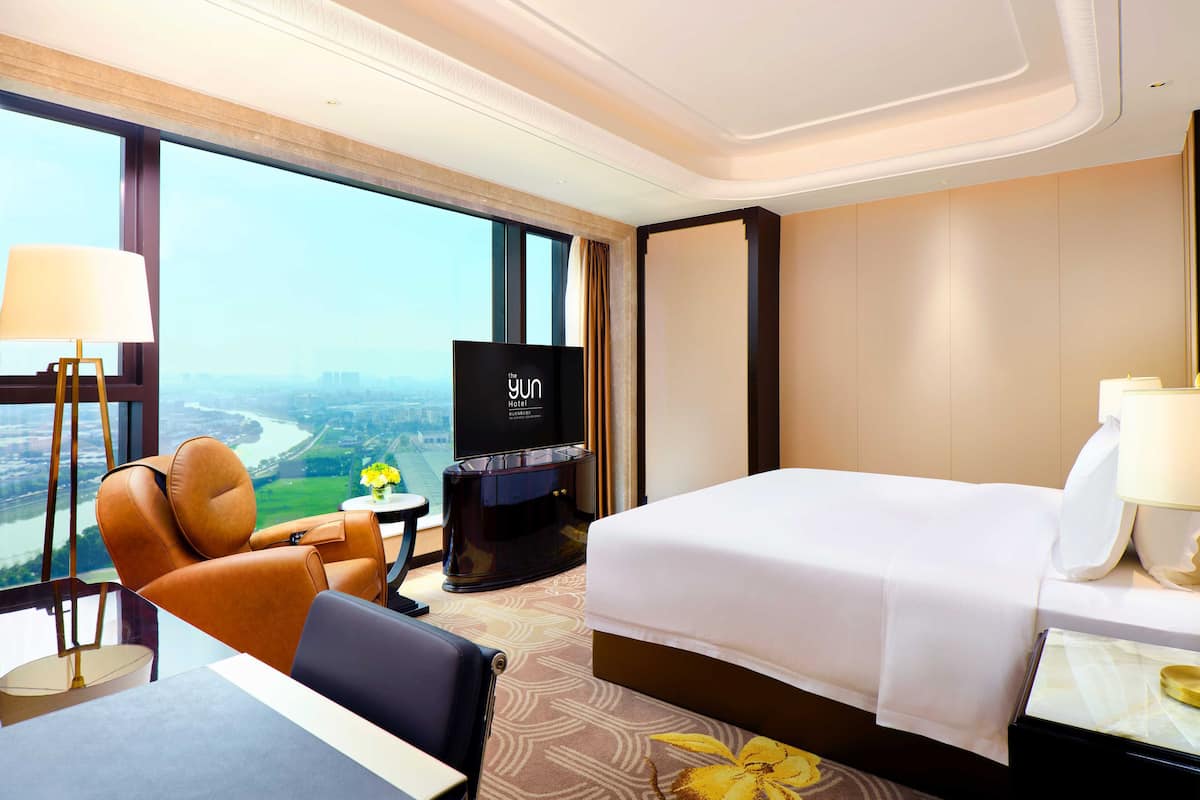 Une chambre d’hôtel avec un grand lit, un bureau, une chaise, une télévision et une vue sur le paysage urbain.