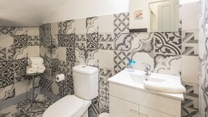 Ein Badezimmer mit gemusterten Fliesen, einer Toilette, einem Waschbecken mit Spiegel und einem Handtuchhalter.