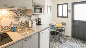 Een compacte keuken met een spoelbak, magnetron en koffiezetapparaat. Er is een klein zitehoekje met een tafel en stoelen.