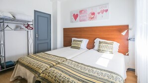 Una cama doble con cabecera de madera, una mesita de noche y un adorno en la pared con corazones y la frase “I love you”.