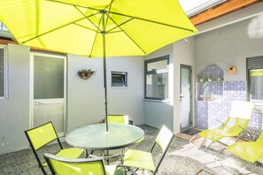 A dining area with a round table, yellow chairs, and a bright yellow umbrella. - Apartamento A Francos Garden Avenue (Porto)