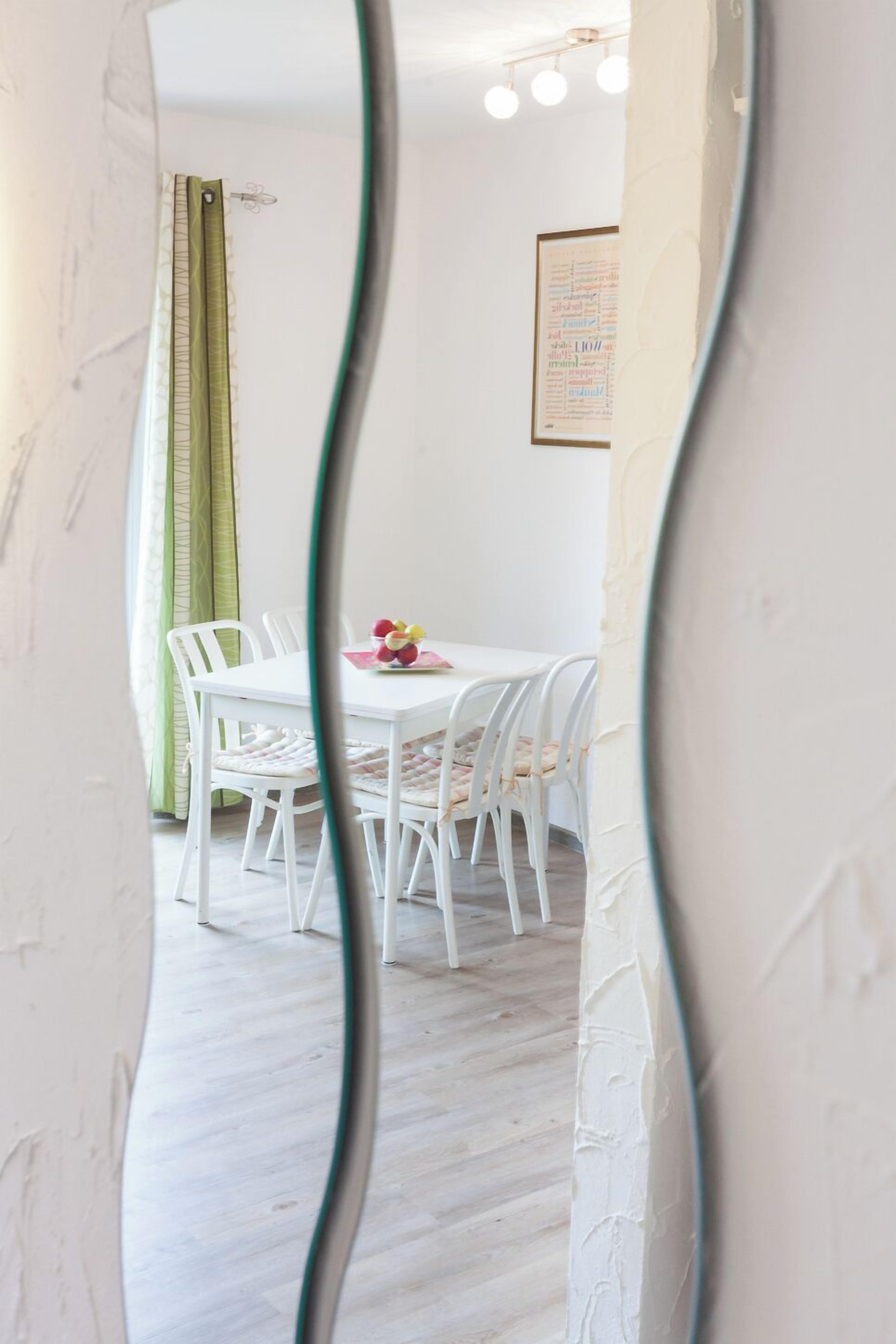 Ein Essbereich mit einem weißen Tisch und Stühlen, einer gerahmten Speisekarte an der Wand und einem grünen Vorhang.