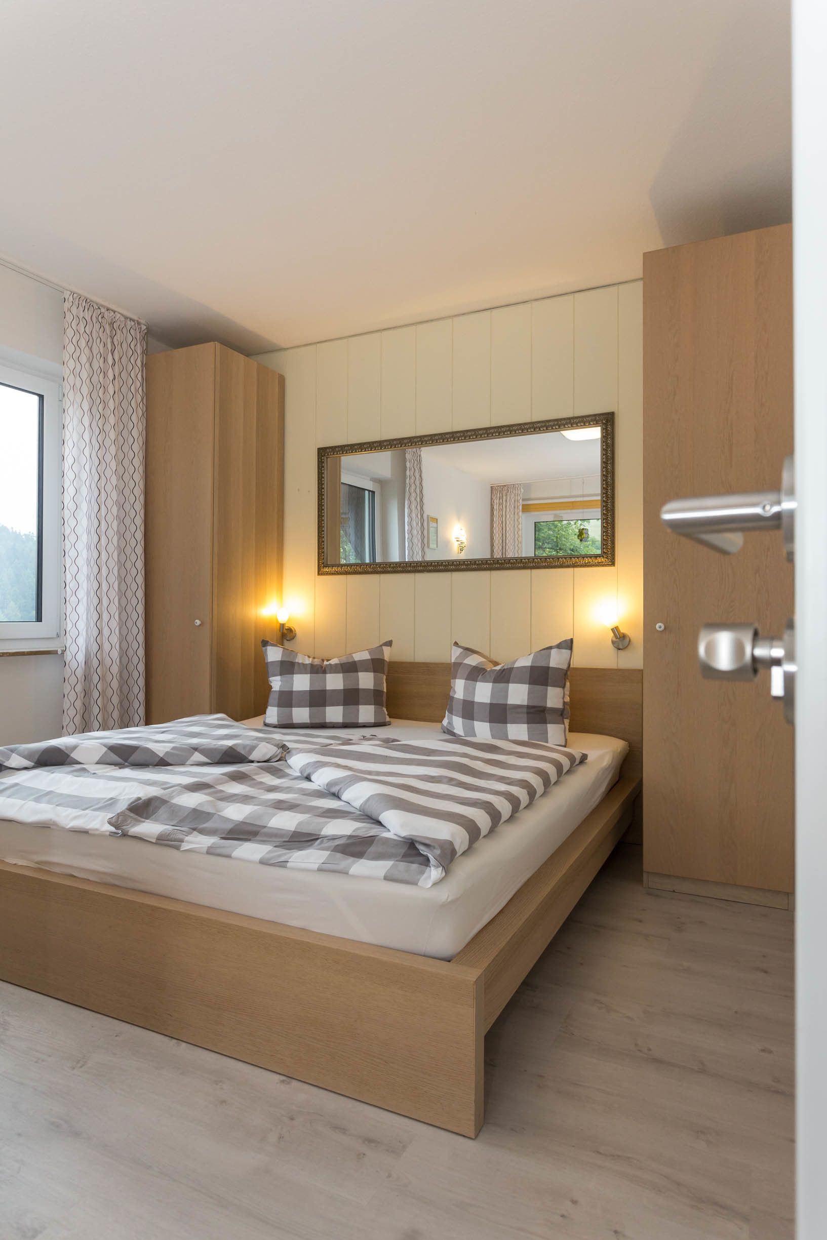 Una camera da letto moderna con un letto a letto in legno, due cuscini, uno specchio e un comodino con una lampada.