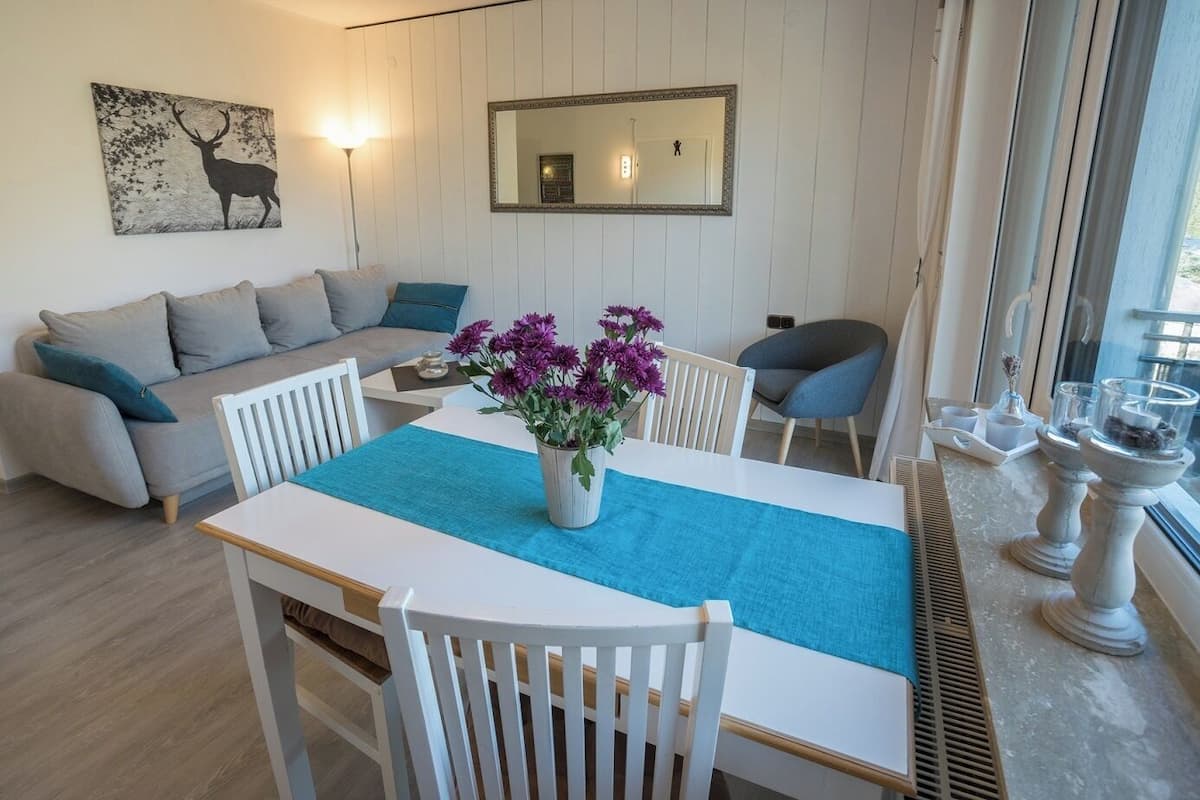 A modern living room with a sofa, dining table, and chairs. There is a vase with flowers on the table.