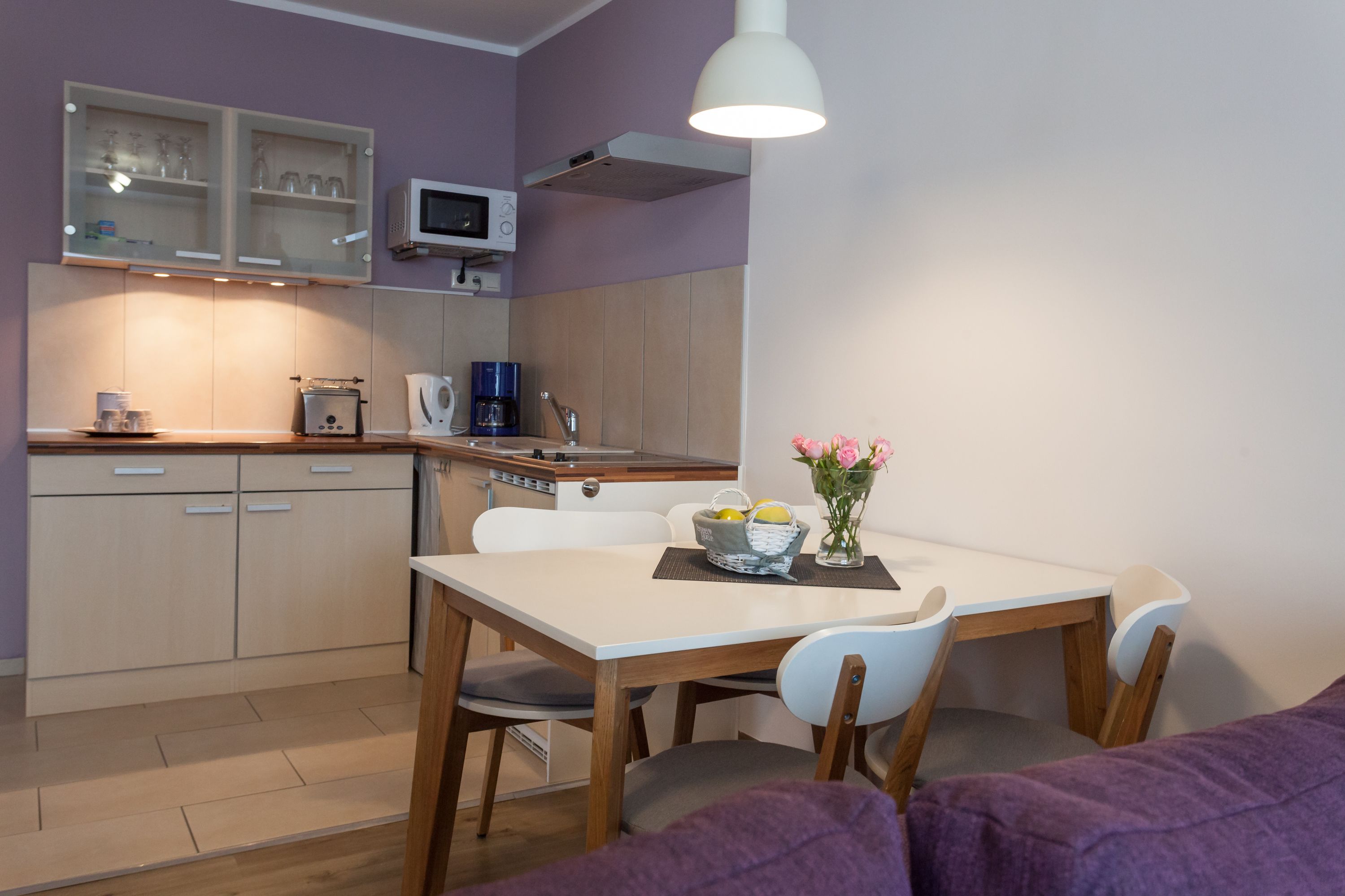 Een kleine keuken met een eethoek, inclusief kastjes, een magnetron, een koffiezetapparaat en een tafel met stoelen.