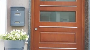 Une porte en bois avec une fente pour le courrier et un pot de fleurs placé à côté.