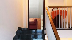 Un escalier avec une rampe en métal, une chaise rouge et une étagère blanche avec des tasses.