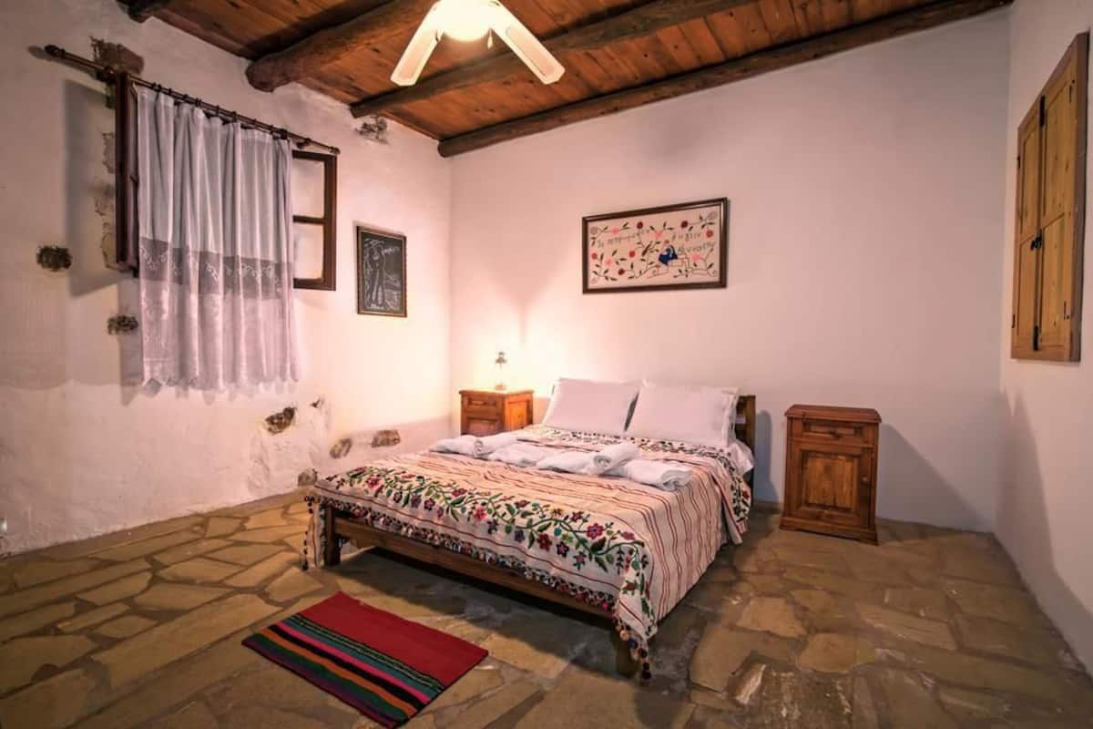 A bedroom with a stone floor, a bed with a floral bedspread, a nightstand, a wooden cabinet, and a wall-mounted picture.
