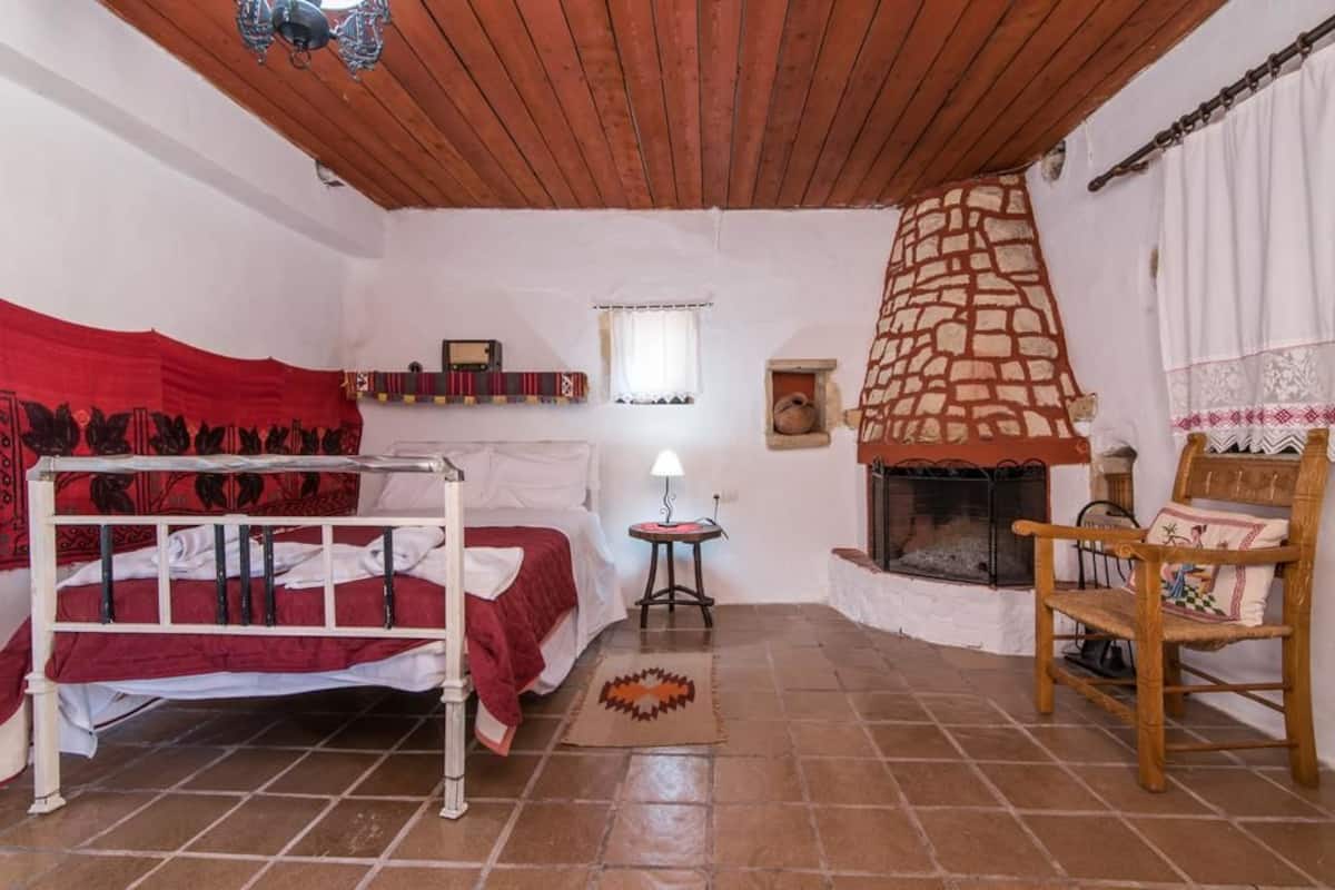 A room with a bed, a small table, a chair, a fireplace, and a window.
