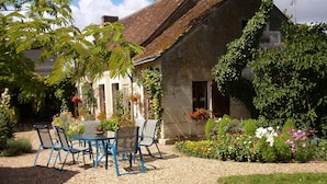 A garden patio with a table and chairs, surrounded by a gravel path and various plants. - Chambres d'hôtes Côté Jardin (Villiers-sur-Loir)