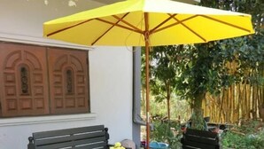 Un espacio al aire libre con dos bancos de madera, una mesa y un paraguas amarillo.