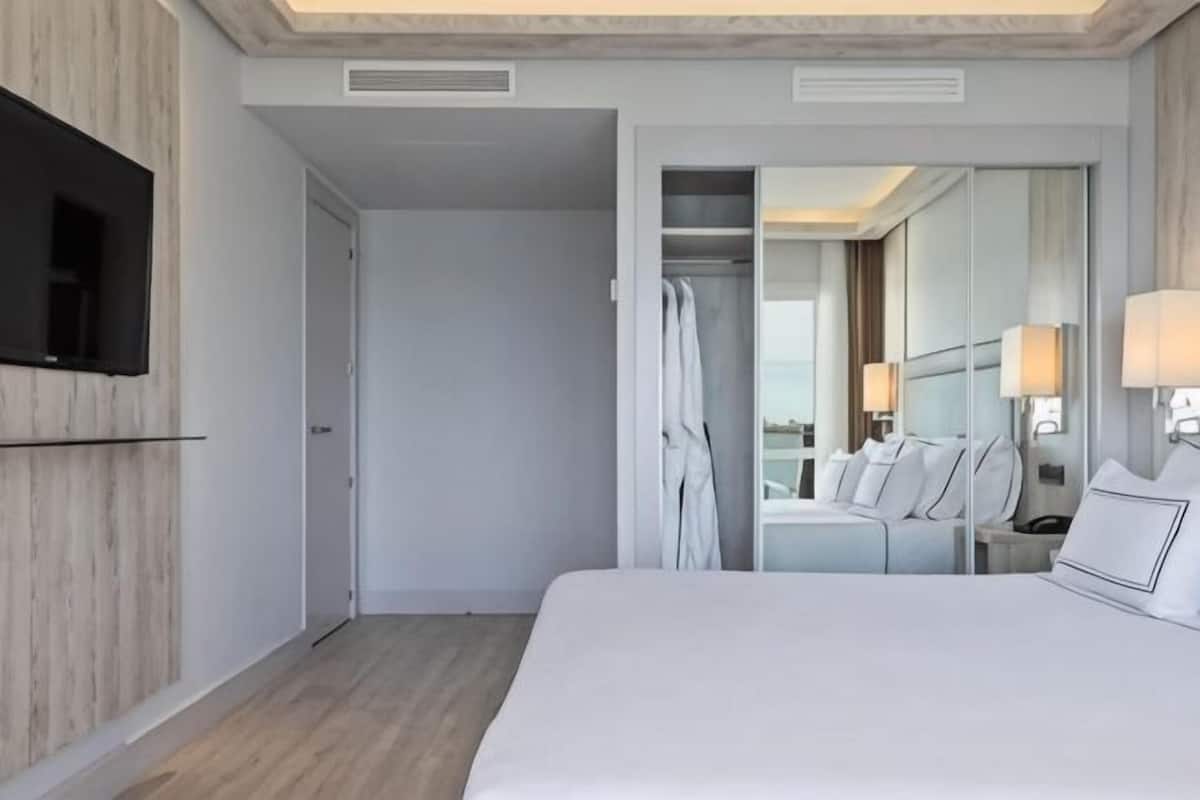Une chambre d’hôtel avec un lit, un téléviseur fixé au mur, une armoire et une salle de bain visible à travers une porte ouverte.