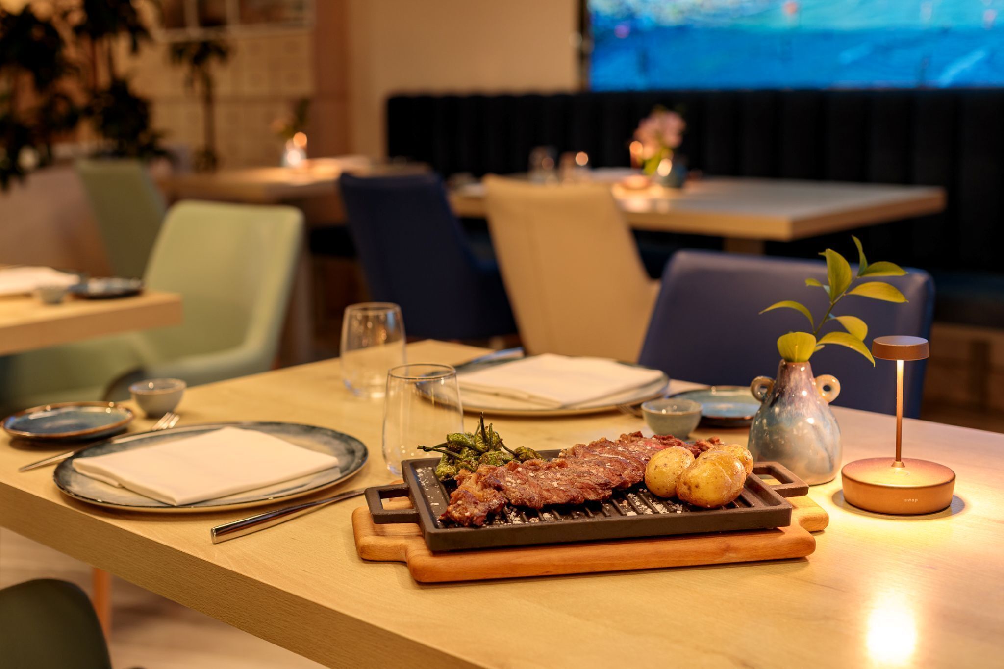 A dining table with a grilled steak, roasted potatoes, and a small vase with a plant.