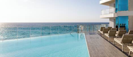 Zona junto a la piscina con vista al océano, sillas de descanso y un flotador.
