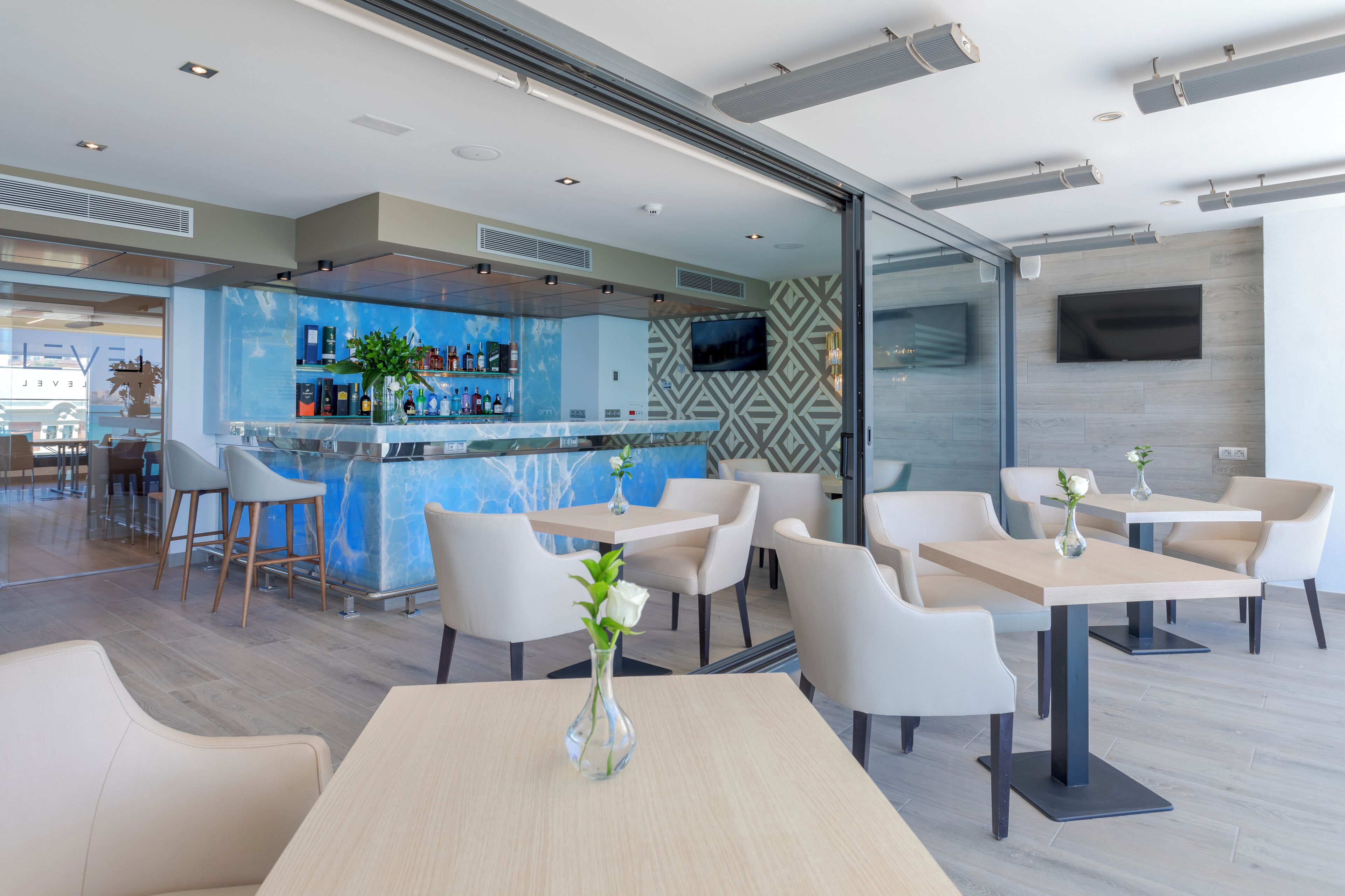 A modern bar area with a blue marble counter, white chairs, and a TV mounted on the wall.