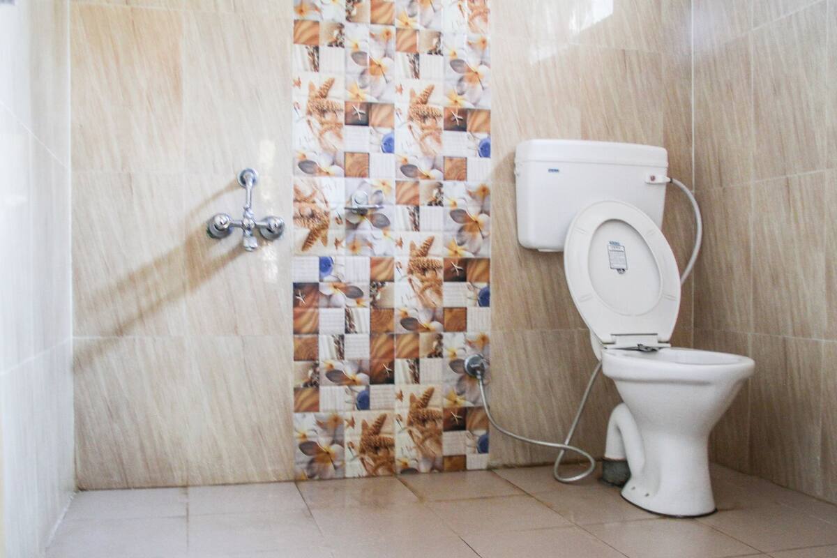 A bathroom with a toilet, a wall-mounted faucet, and a tiled wall with a floral pattern.