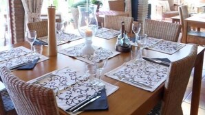 Un coin repas avec une table en bois dressée pour quatre personnes, entourée de chaises en osier. Une lanterne décorative est suspendue au-dessus de la table.