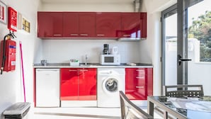 A compact kitchen with red cabinets, a washing machine, a microwave, and a coffee maker. - Apartamento A Francos Balcony (Porto)