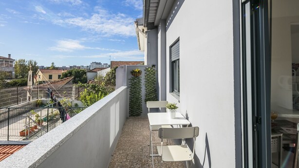 A balcony with a white table and chairs, a small potted plant, and a view of the cityscape. - Apartamento A Francos Balcony (Porto)