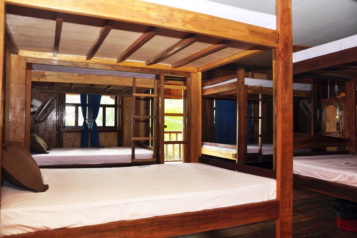 A rustic wooden room with bunk beds and a staircase leading to an upper level.