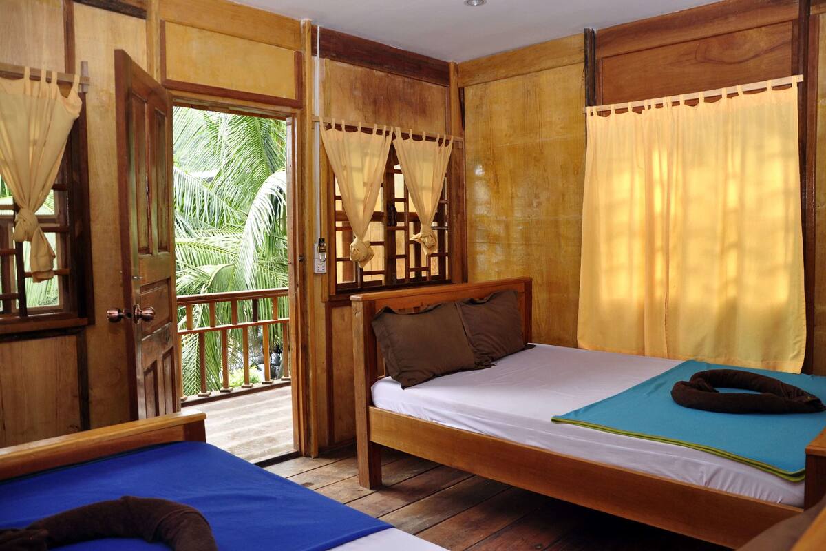 A wooden room with a bed, a small table, and a window with curtains.