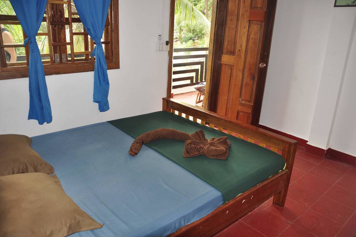 A single bed with a green mattress, a brown blanket, and a brown towel.
