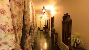 A hallway with floral curtains, a wooden cabinet, and potted plants. - Vijaigarh kothi (Varanasi)