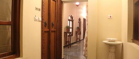 Un pasillo con puertas de madera, un pedestal blanco y un piso de baldosas.