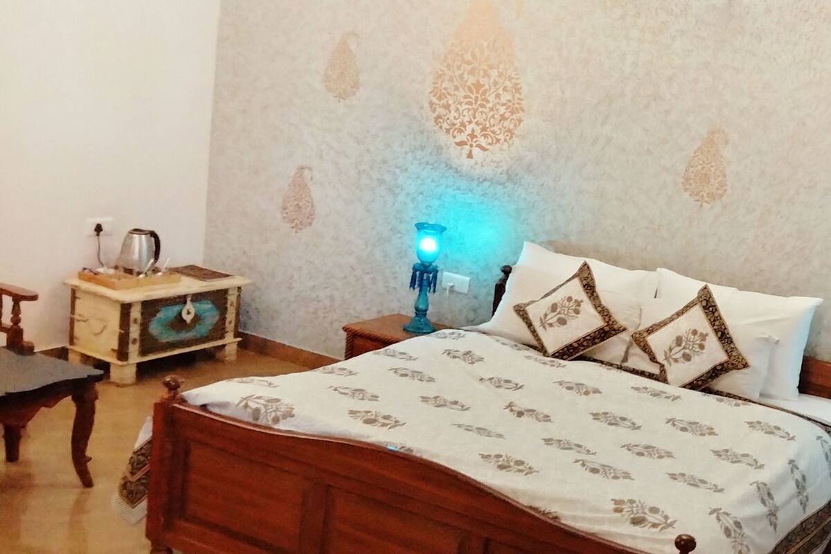 A bedroom with a wooden bed, patterned bedding, two bedside lamps, a nightstand, a small table, and a wall with decorative patterns.