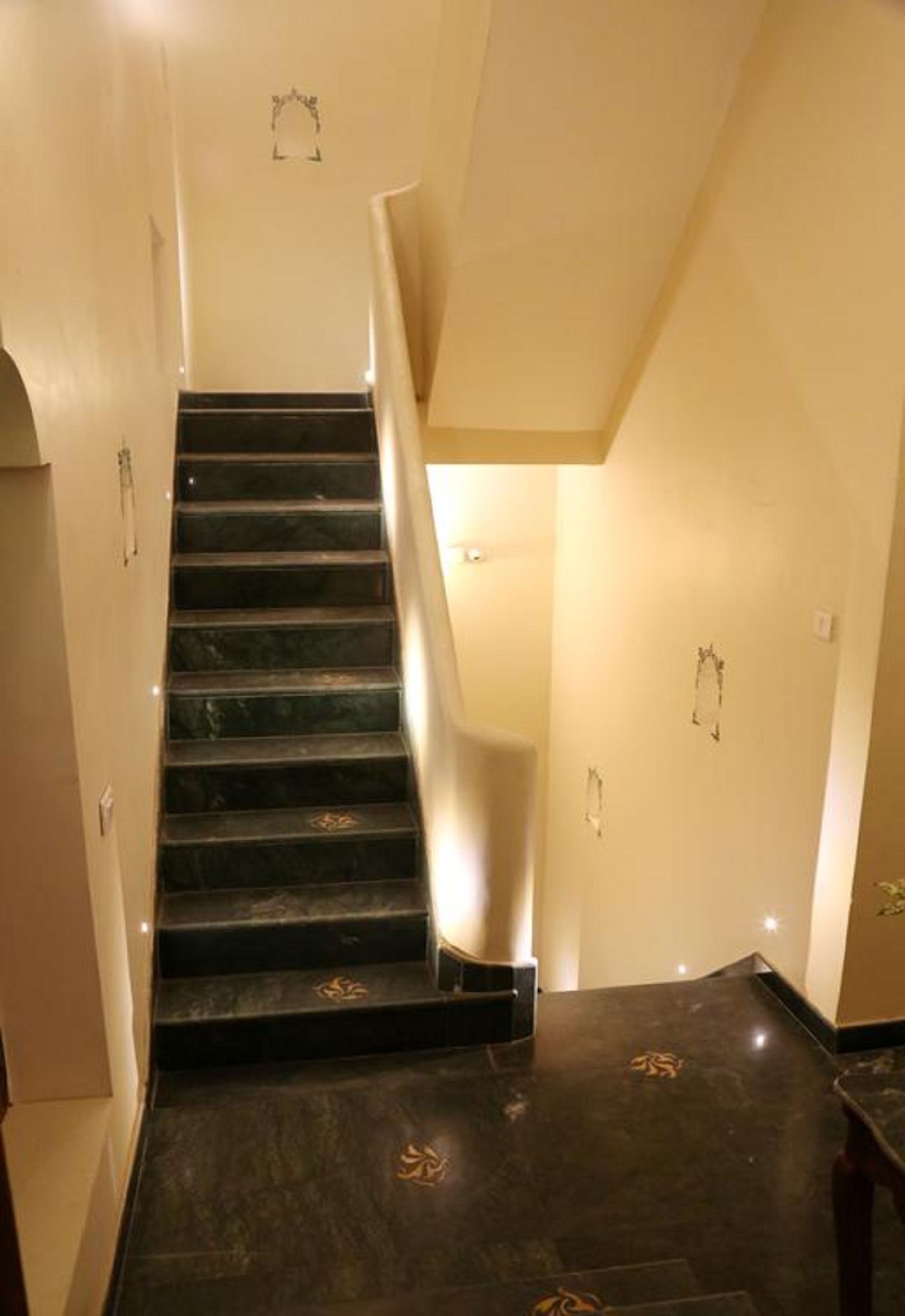Eine Treppe mit dunklen Marmorstufen und einem Geländer, die zu einer Zwischenebene mit einer Leuchte führt.