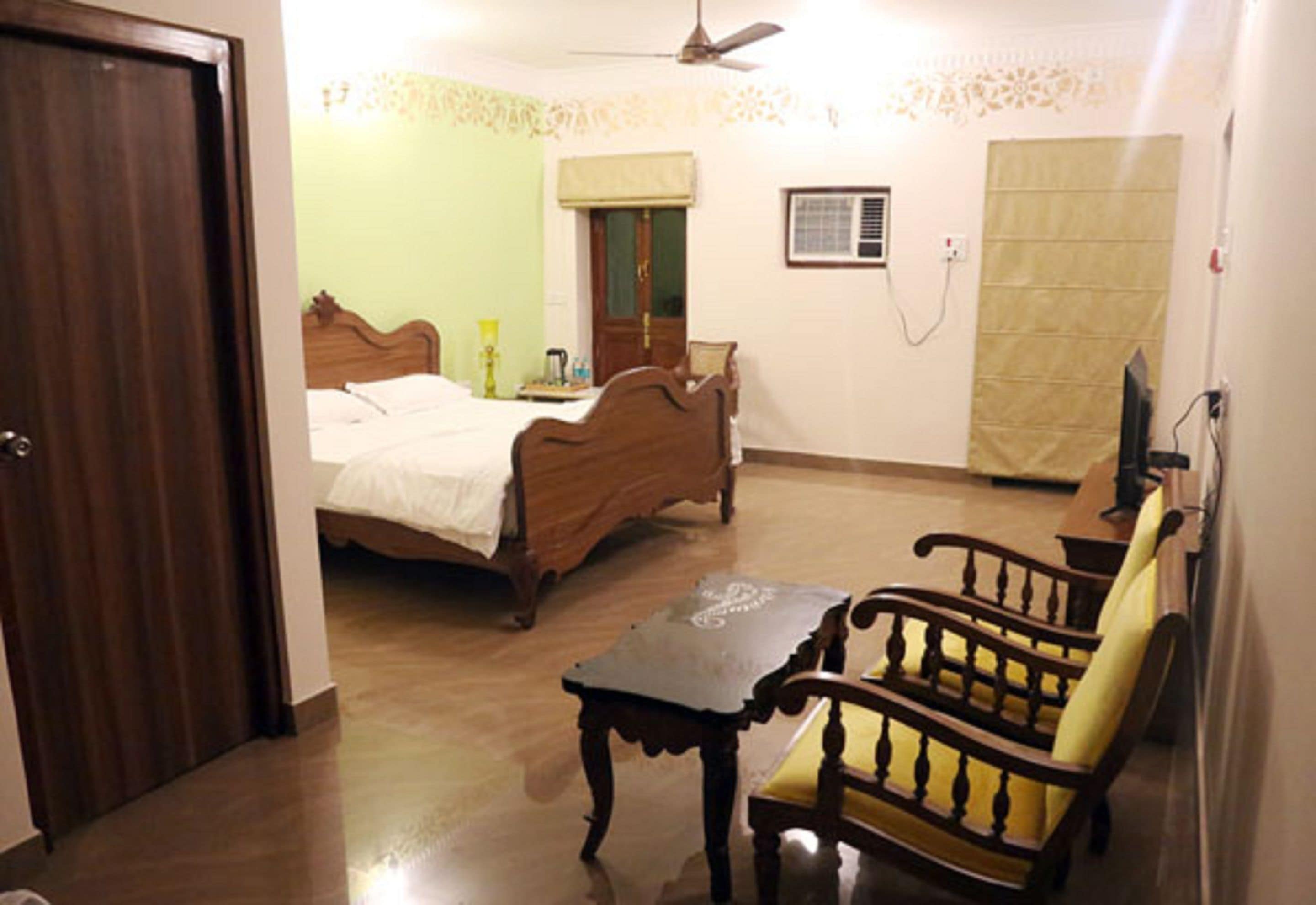 A bedroom with a wooden bed, a wooden chair, a small table, a ceiling fan, and a window with a curtain.
