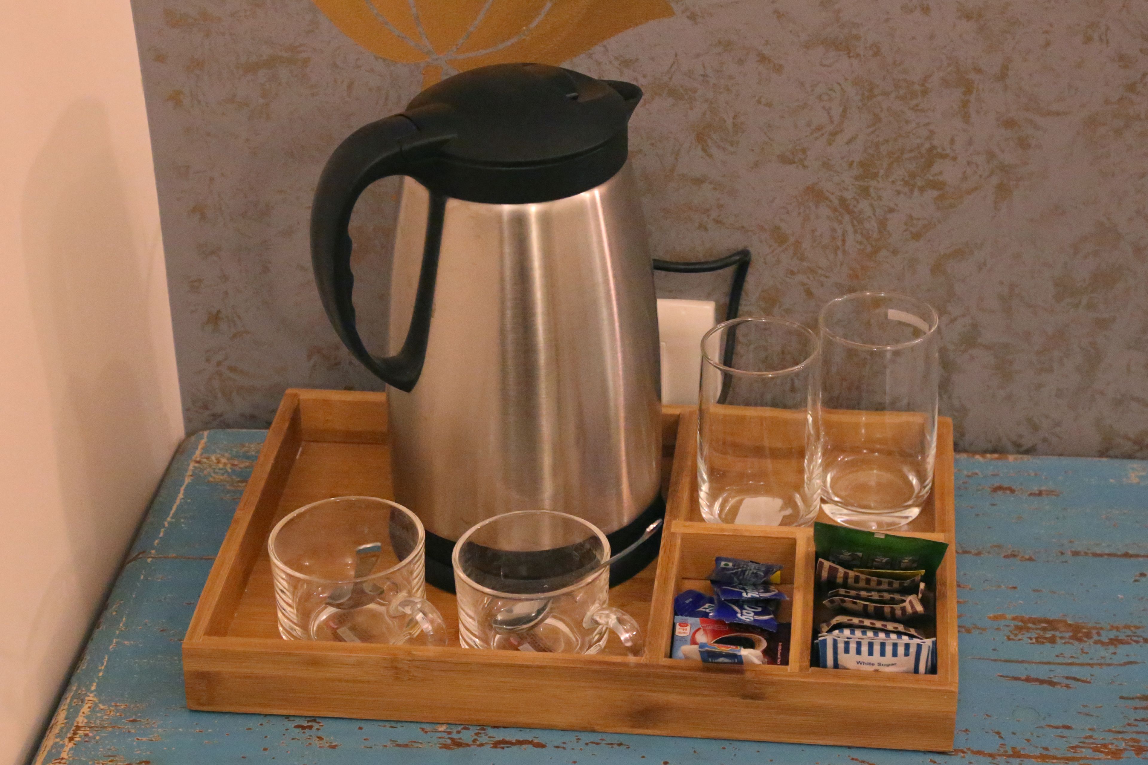 A stainless steel coffee pot on a wooden tray with four glasses and a small compartment with packets.