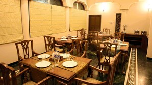 A dining area with multiple wooden tables and chairs, arranged in a spacious room with patterned walls and a chandelier. - Vijaigarh kothi (Varanasi)