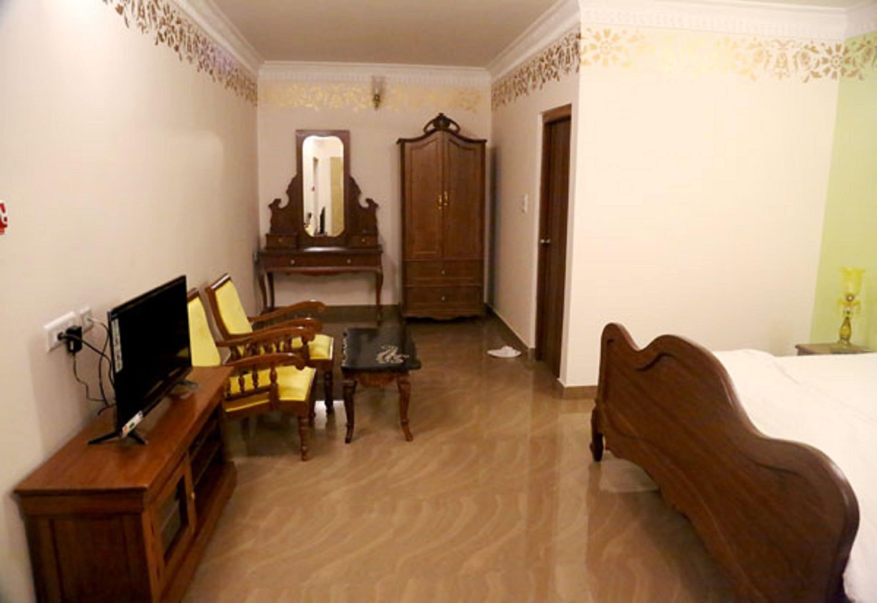 A room with a bed, a wooden wardrobe, a desk with a chair, a television, and a mirror.