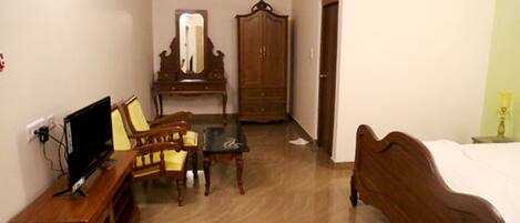 A room with a bed, a wooden wardrobe, a desk with a chair, a television, and a mirror.
