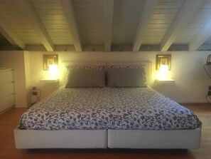 A bedroom with a bed, two bedside lamps, and a ceiling with wooden beams.