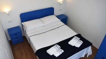 A neatly made bed with white linens and a black bedspread, two blue nightstands with drawers, and a wall-mounted light fixture.