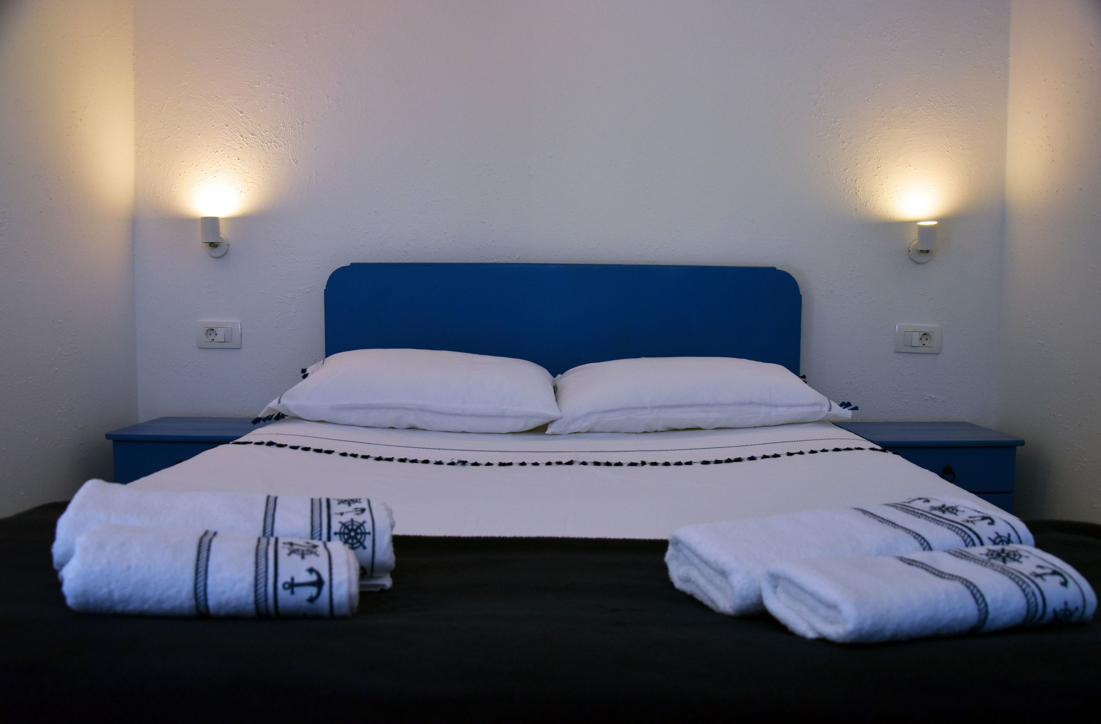 A bed with white linens and two pillows, flanked by two nightstands with wall-mounted lamps.