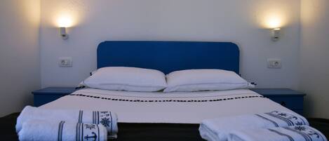 A bed with white linens and two pillows, flanked by two nightstands with wall-mounted lamps.