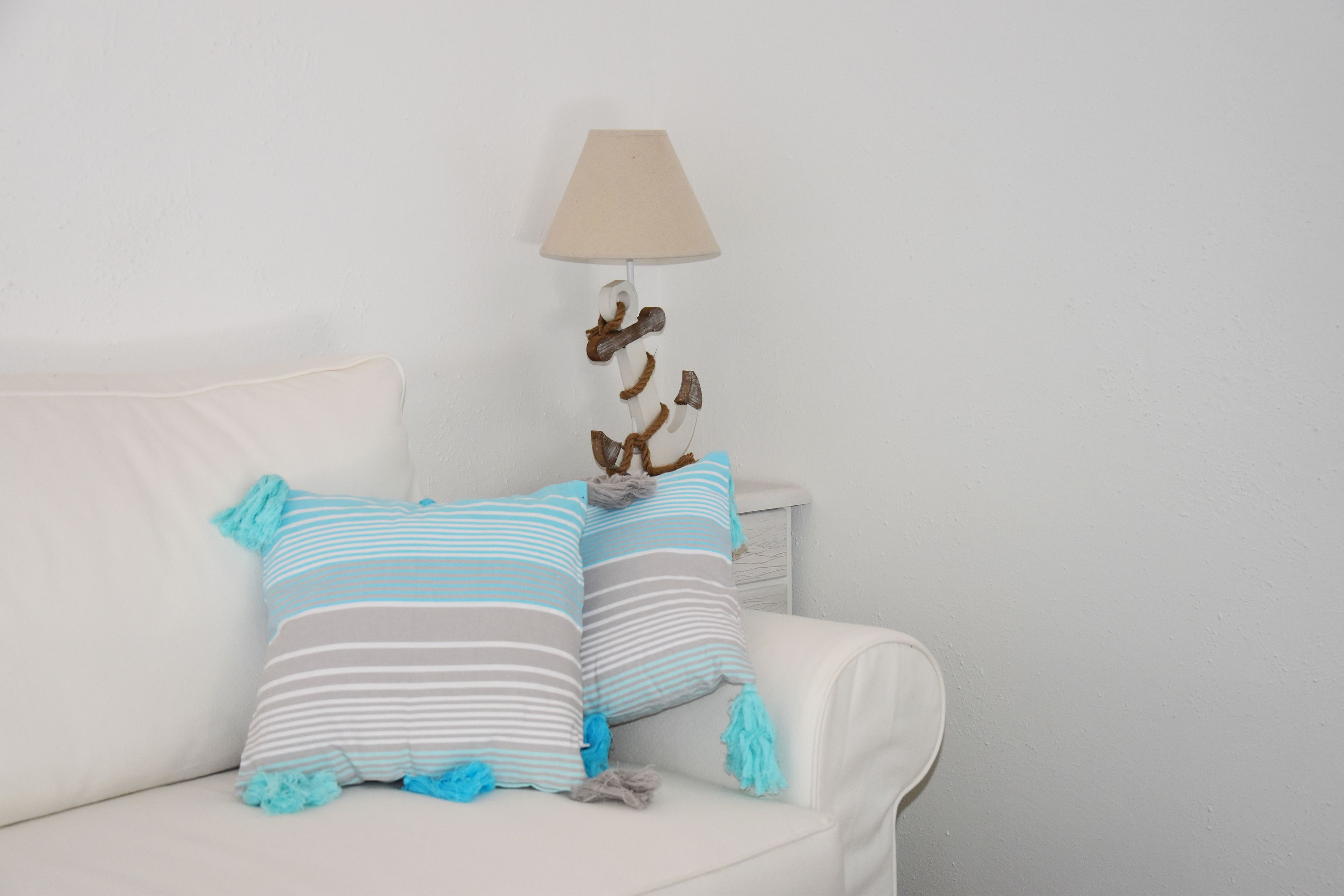 A white sofa with striped pillows and a hanging lamp.